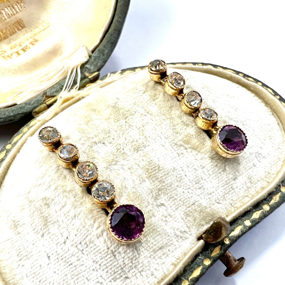 A pair of Edwardian 9ct yellow gold drop earrings with linear clear stones and round purple amethyst terminals set in a green fitted display box. View II