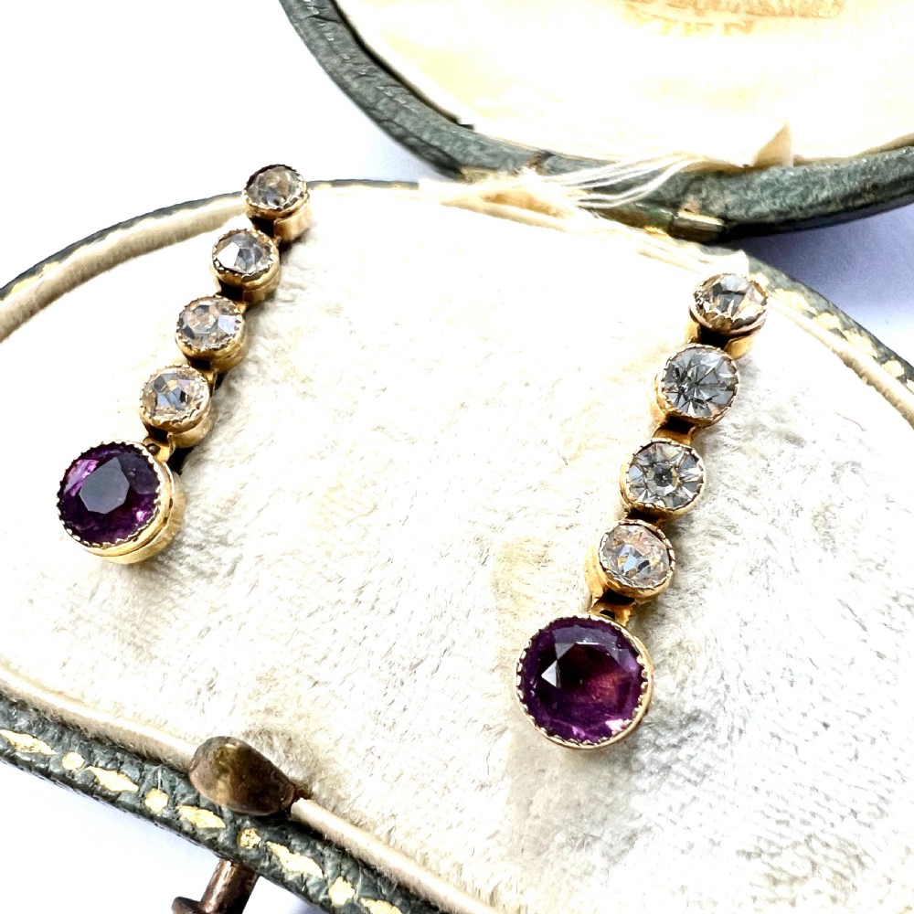 A pair of Edwardian 9ct yellow gold drop earrings with linear clear stones and round purple amethyst terminals set in a green fitted display box. View III
