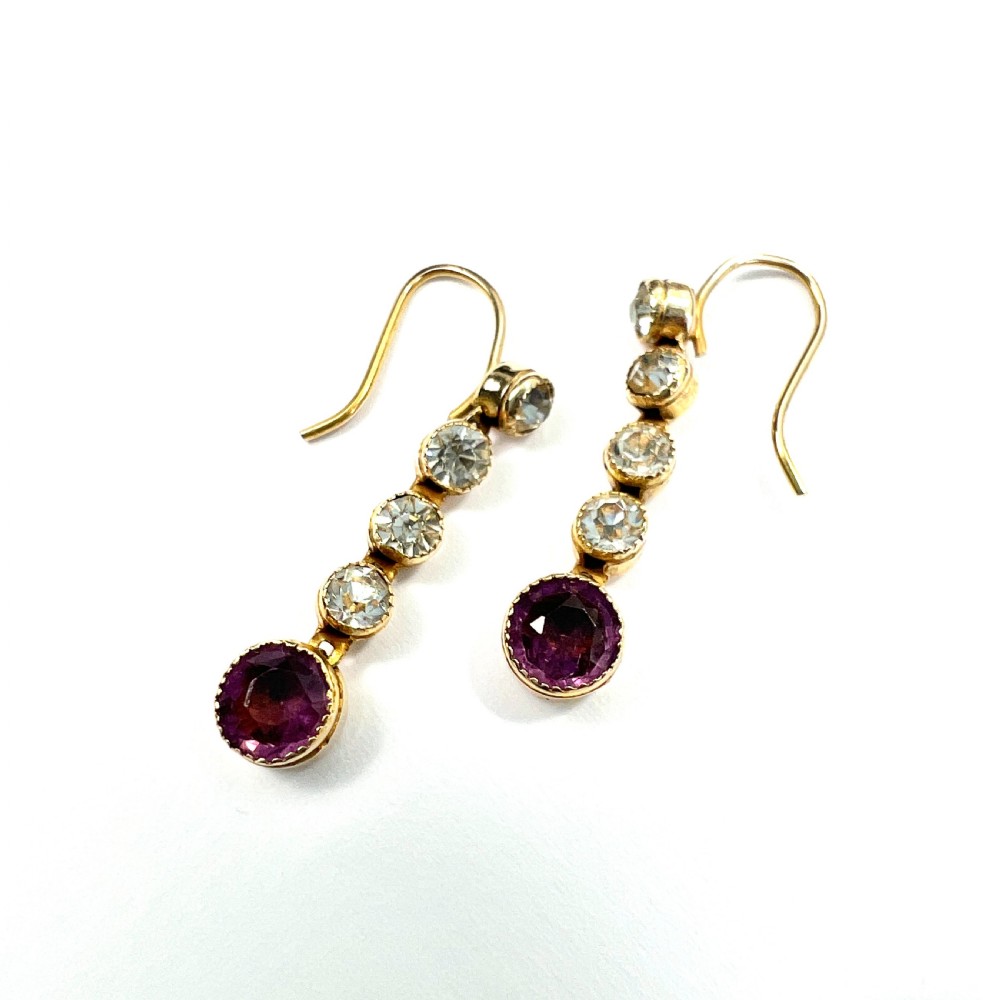 A pair of Edwardian 9ct yellow gold drop earrings with linear clear stones and round purple amethyst terminals set in a green fitted display box. View IV