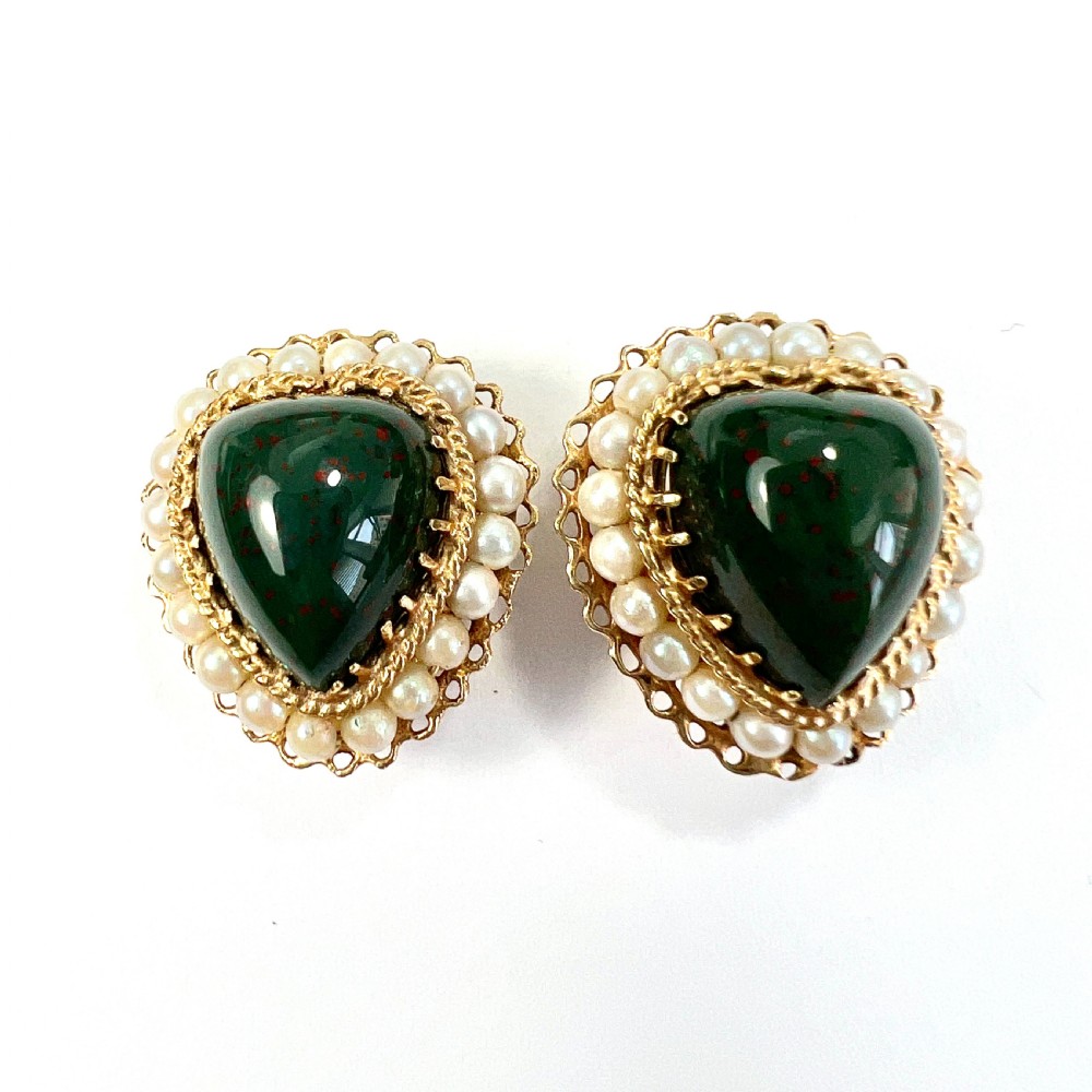 A pair of heart-shaped dark green bloodstone cabochon clip earrings framed by 14ct gold filigree and a halo of white seed pearls.