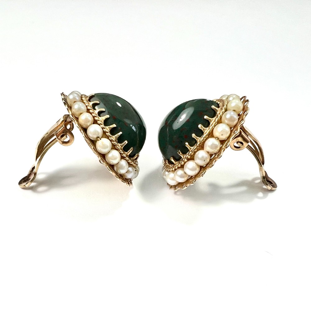 A pair of heart-shaped dark green bloodstone cabochon clip earrings framed by 14ct gold filigree and a halo of white seed pearls. View IV