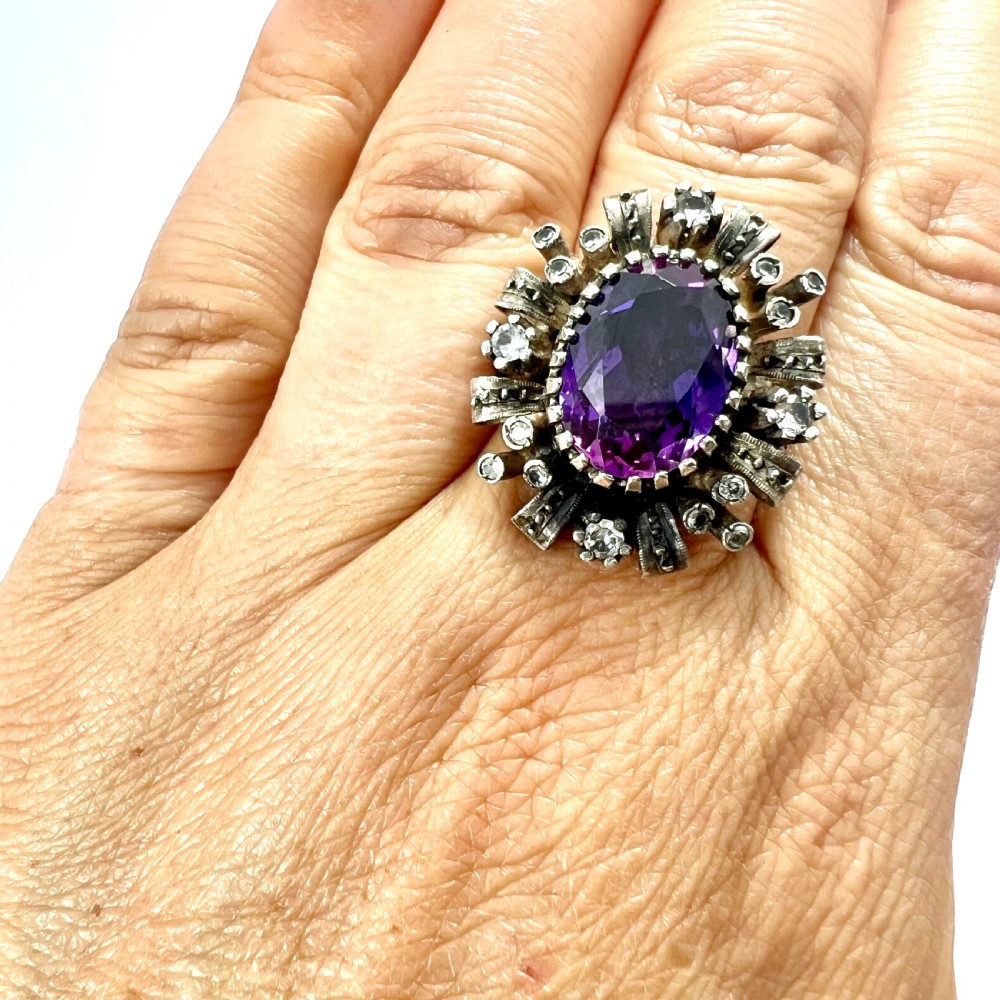 A three-piece jewellery suite featuring a oval purple gemstone ring and matching cluster earrings in silver and gold settings. View VII