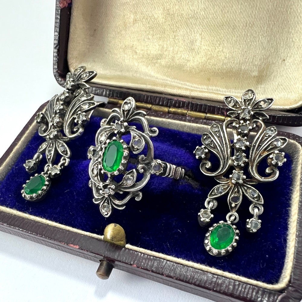 A vintage silver jewellery set featuring a pair of foliate drop earrings and a matching ring, each set with green paste emeralds and clear glass stones. View II