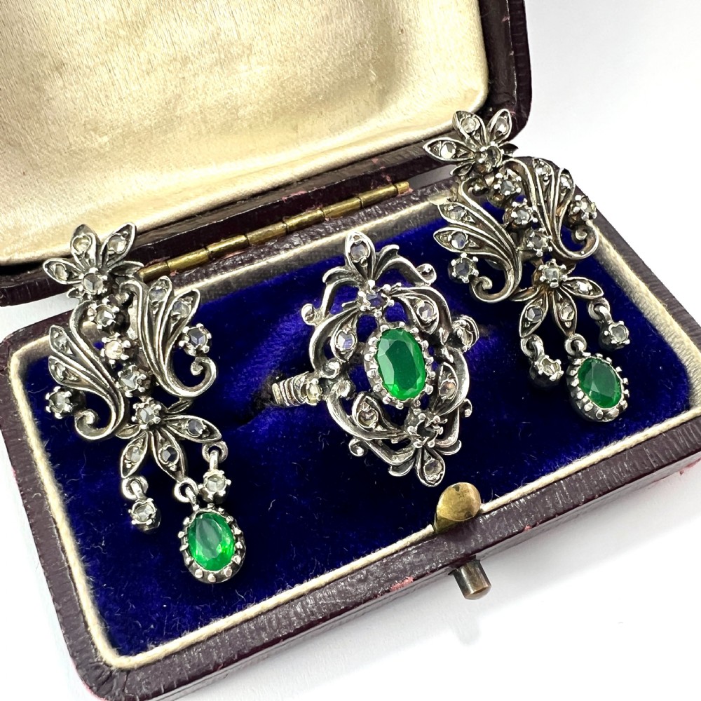A vintage silver jewellery set featuring a pair of foliate drop earrings and a matching ring, each set with green paste emeralds and clear glass stones. View III