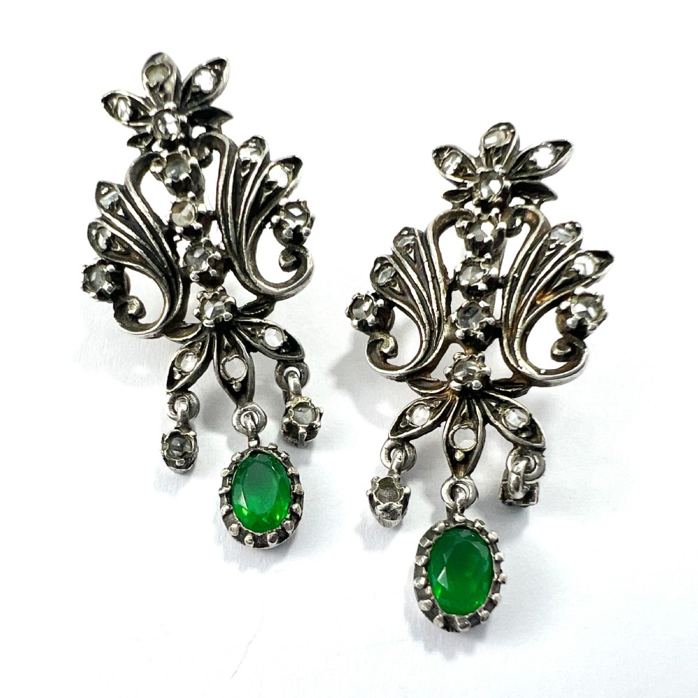 A vintage silver jewellery set featuring a pair of foliate drop earrings and a matching ring, each set with green paste emeralds and clear glass stones. View IV