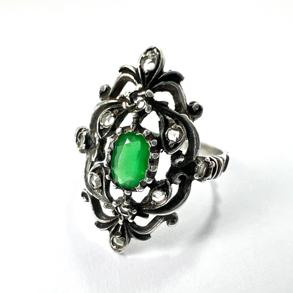 A vintage silver jewellery set featuring a pair of foliate drop earrings and a matching ring, each set with green paste emeralds and clear glass stones. View V