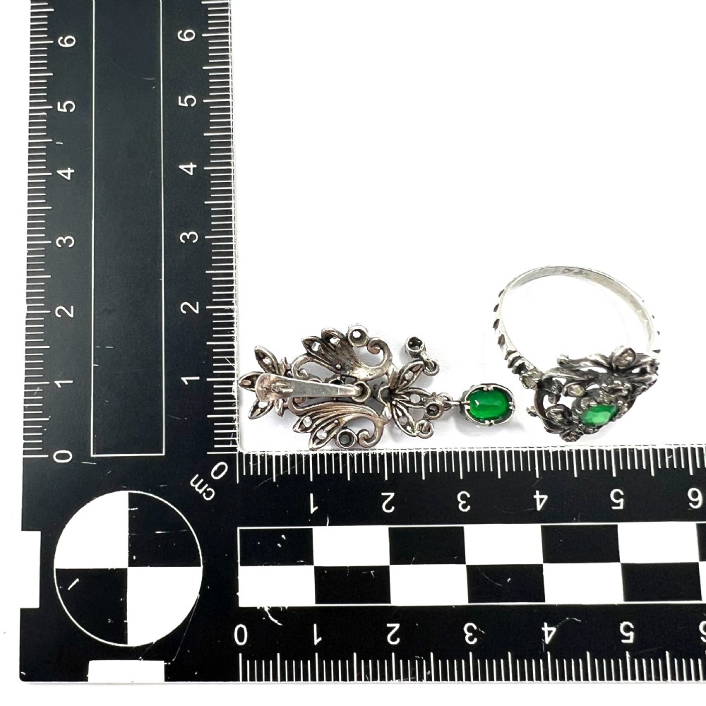 A vintage silver jewellery set featuring a pair of foliate drop earrings and a matching ring, each set with green paste emeralds and clear glass stones. View VII