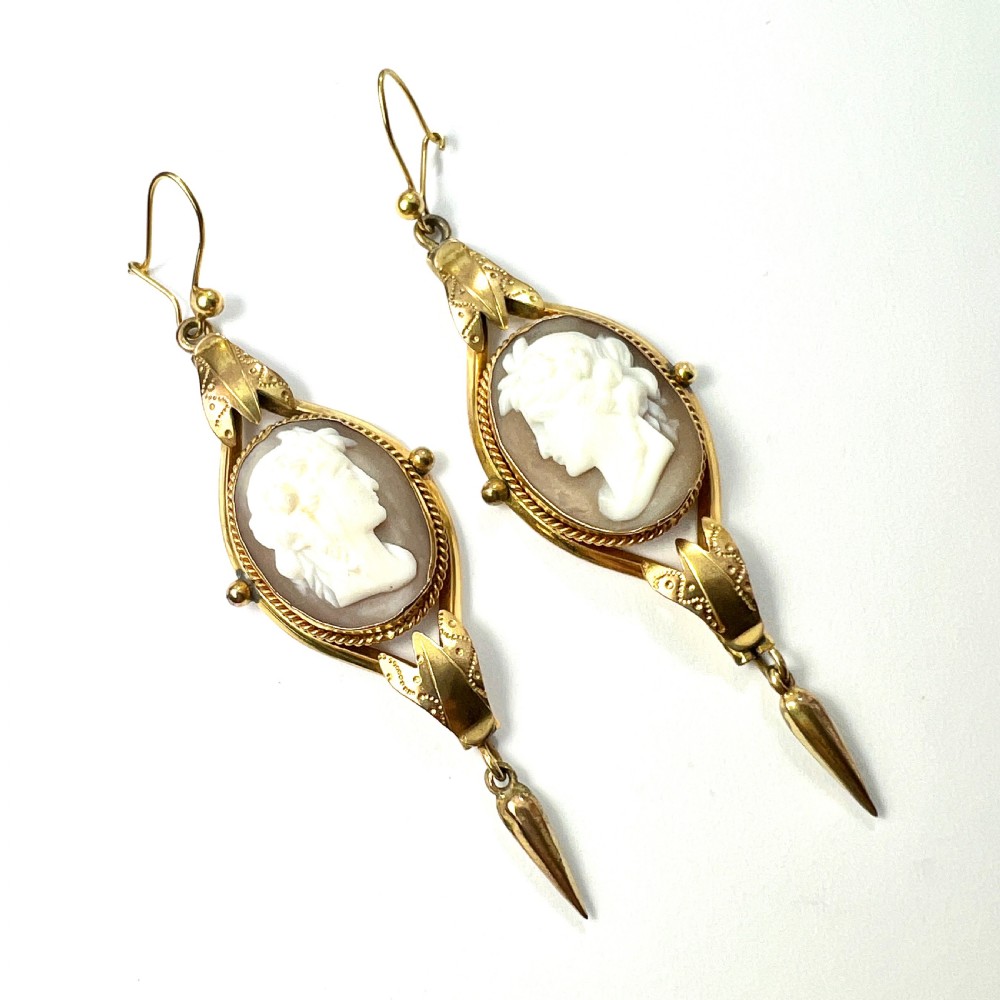 A pair of Victorian drop earrings featuring oval carved shell cameos set in pinchbeck frames with engraved leaf details and 9ct gold ear wires.