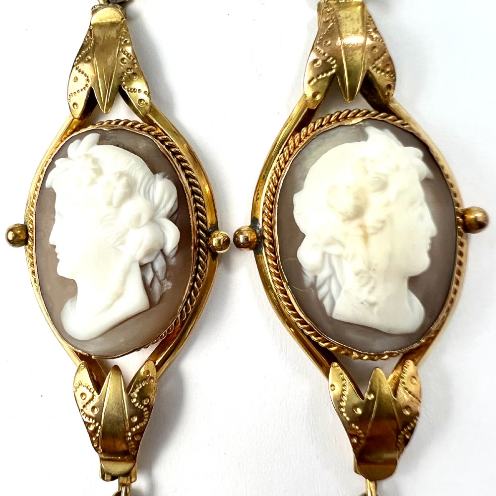 A pair of Victorian drop earrings featuring oval carved shell cameos set in pinchbeck frames with engraved leaf details and 9ct gold ear wires. View V