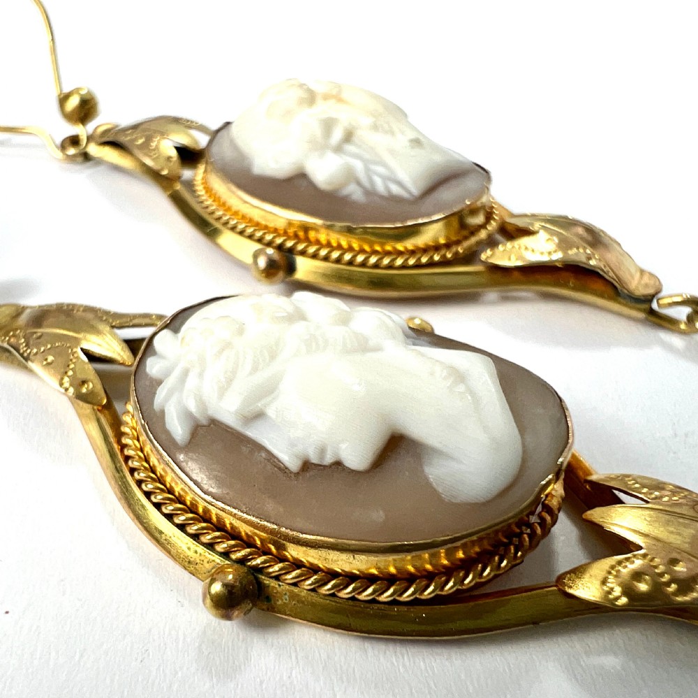 A pair of Victorian drop earrings featuring oval carved shell cameos set in pinchbeck frames with engraved leaf details and 9ct gold ear wires. View VI