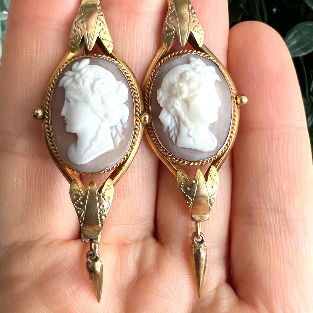A pair of Victorian drop earrings featuring oval carved shell cameos set in pinchbeck frames with engraved leaf details and 9ct gold ear wires. View IX