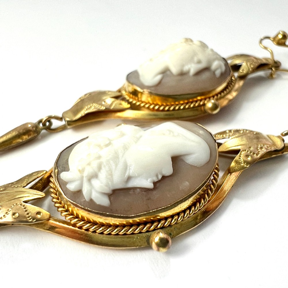 A pair of Victorian drop earrings featuring oval carved shell cameos set in pinchbeck frames with engraved leaf details and 9ct gold ear wires. View X