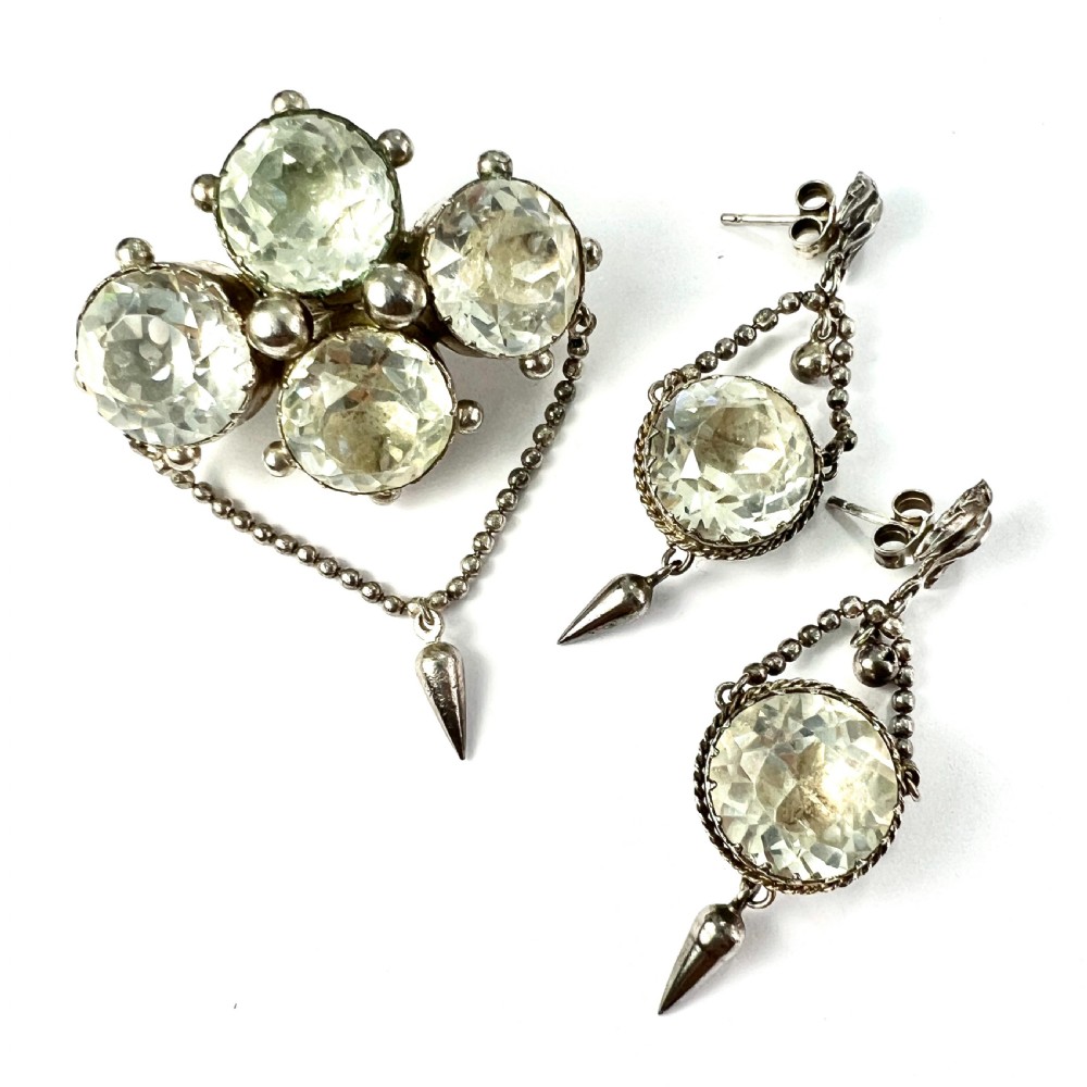 An antique silver demi-parure featuring round clear foiled paste stones in closed collet settings, comprising dangle earrings with cone drops and a matching cluster brooch with a draped beaded chain. View II