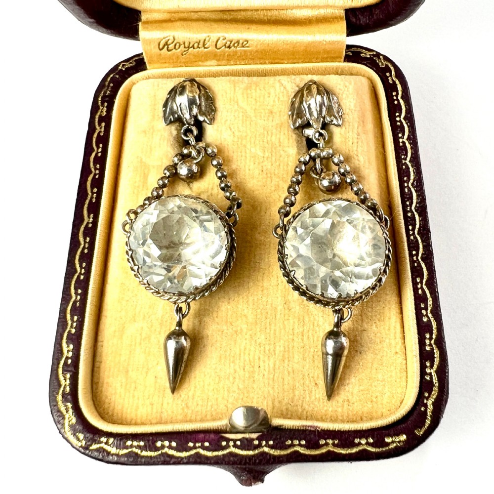 An antique silver demi-parure featuring round clear foiled paste stones in closed collet settings, comprising dangle earrings with cone drops and a matching cluster brooch with a draped beaded chain. View V