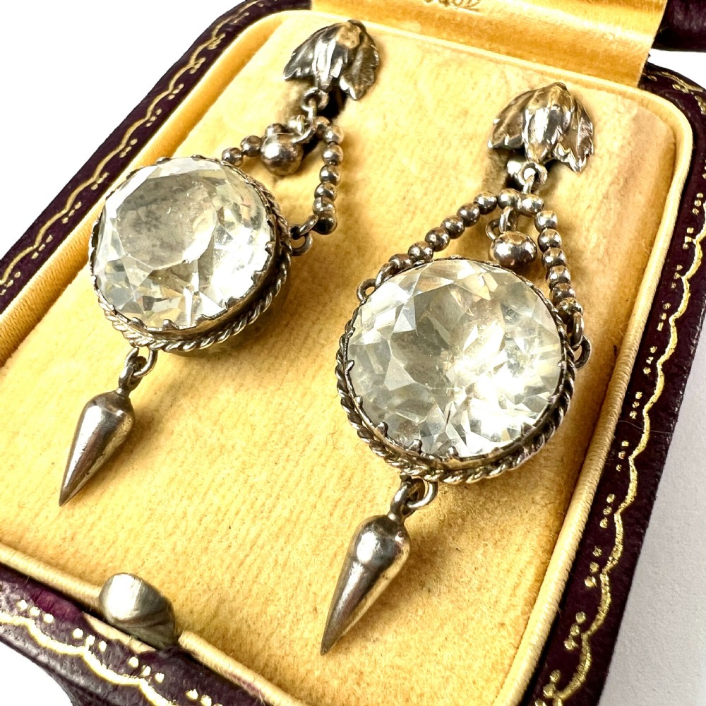 An antique silver demi-parure featuring round clear foiled paste stones in closed collet settings, comprising dangle earrings with cone drops and a matching cluster brooch with a draped beaded chain. View VI