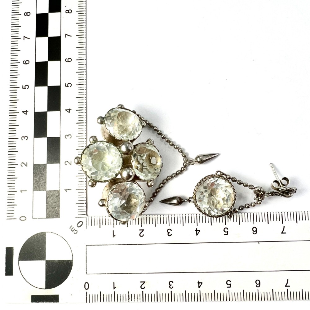 An antique silver demi-parure featuring round clear foiled paste stones in closed collet settings, comprising dangle earrings with cone drops and a matching cluster brooch with a draped beaded chain. View VII