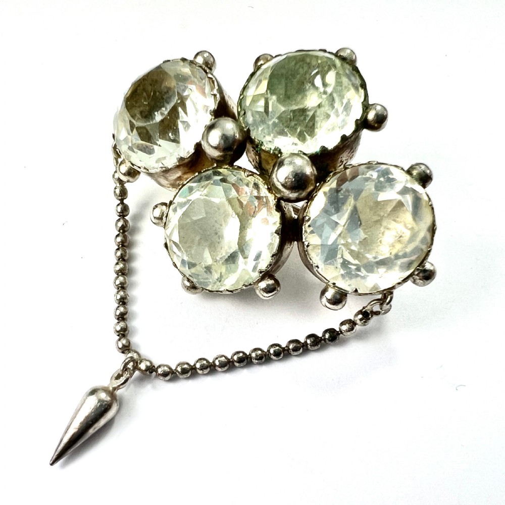 An antique silver demi-parure featuring round clear foiled paste stones in closed collet settings, comprising dangle earrings with cone drops and a matching cluster brooch with a draped beaded chain. View X