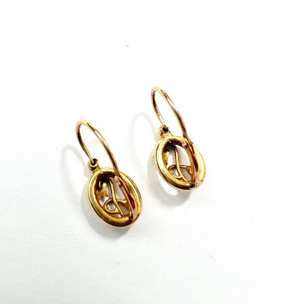 A pair of 9ct yellow gold Art Nouveau dormeuse earrings featuring an oval frame enclosing a botanical scroll motif with a seed pearl accent. View IV