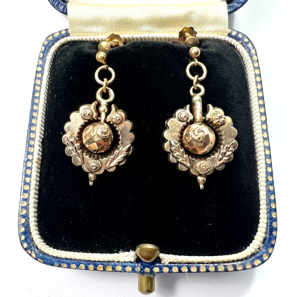 A pair of Victorian 9ct gold drop earrings featuring scalloped borders and central spherical motifs, displayed in a navy blue velvet jewellery box.