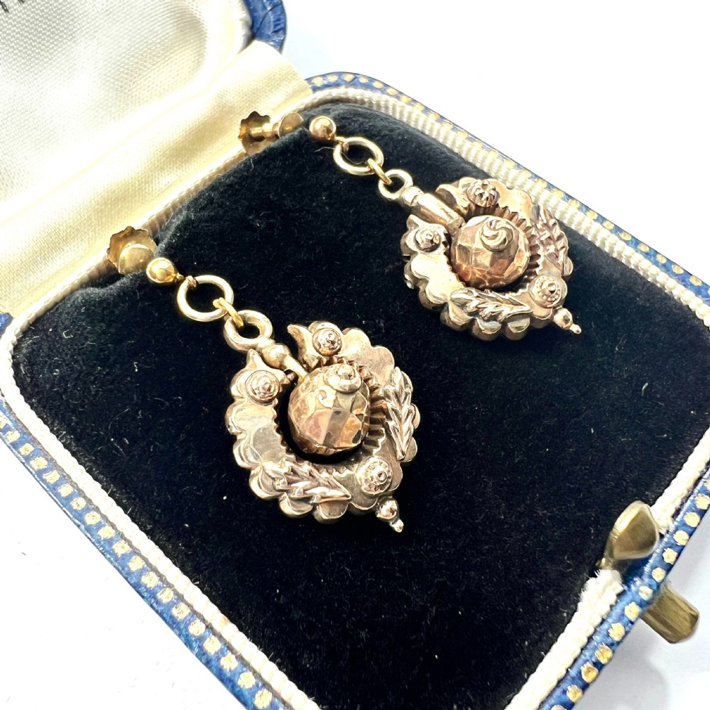 A pair of Victorian 9ct gold drop earrings featuring scalloped borders and central spherical motifs, displayed in a navy blue velvet jewellery box. View II
