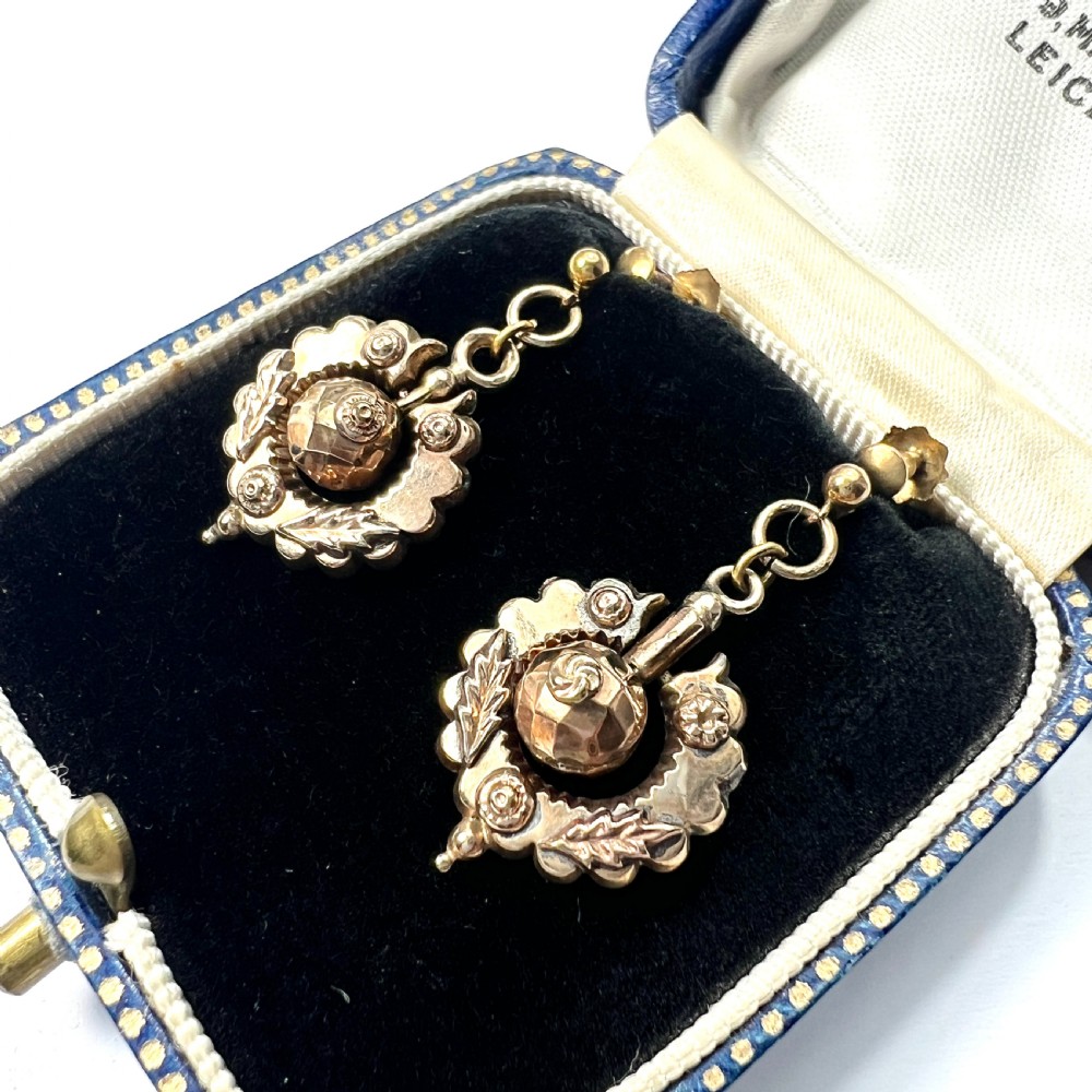 A pair of Victorian 9ct gold drop earrings featuring scalloped borders and central spherical motifs, displayed in a navy blue velvet jewellery box. View III