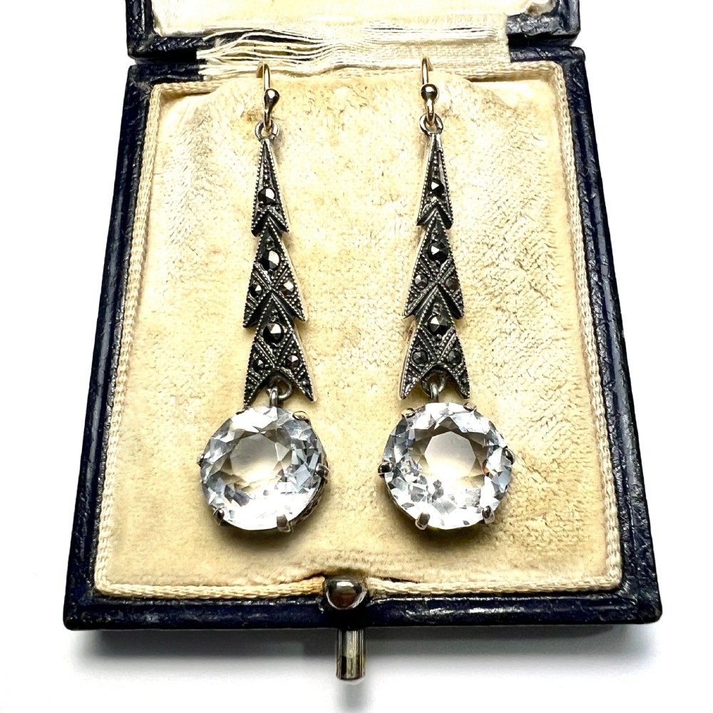 Art Deco silver drop earrings featuring geometric marcasite-set chevron panels above large round faceted clear zircon stones.