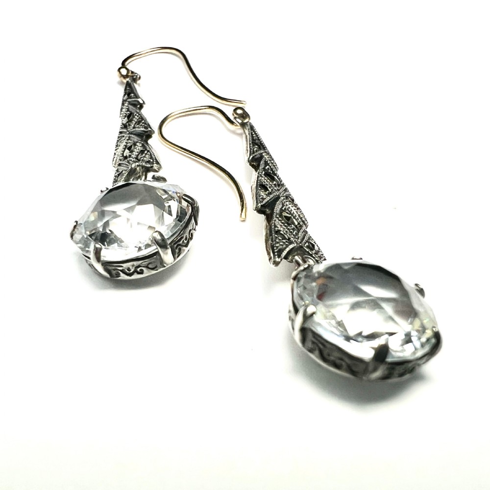 Art Deco silver drop earrings featuring geometric marcasite-set chevron panels above large round faceted clear zircon stones. View V
