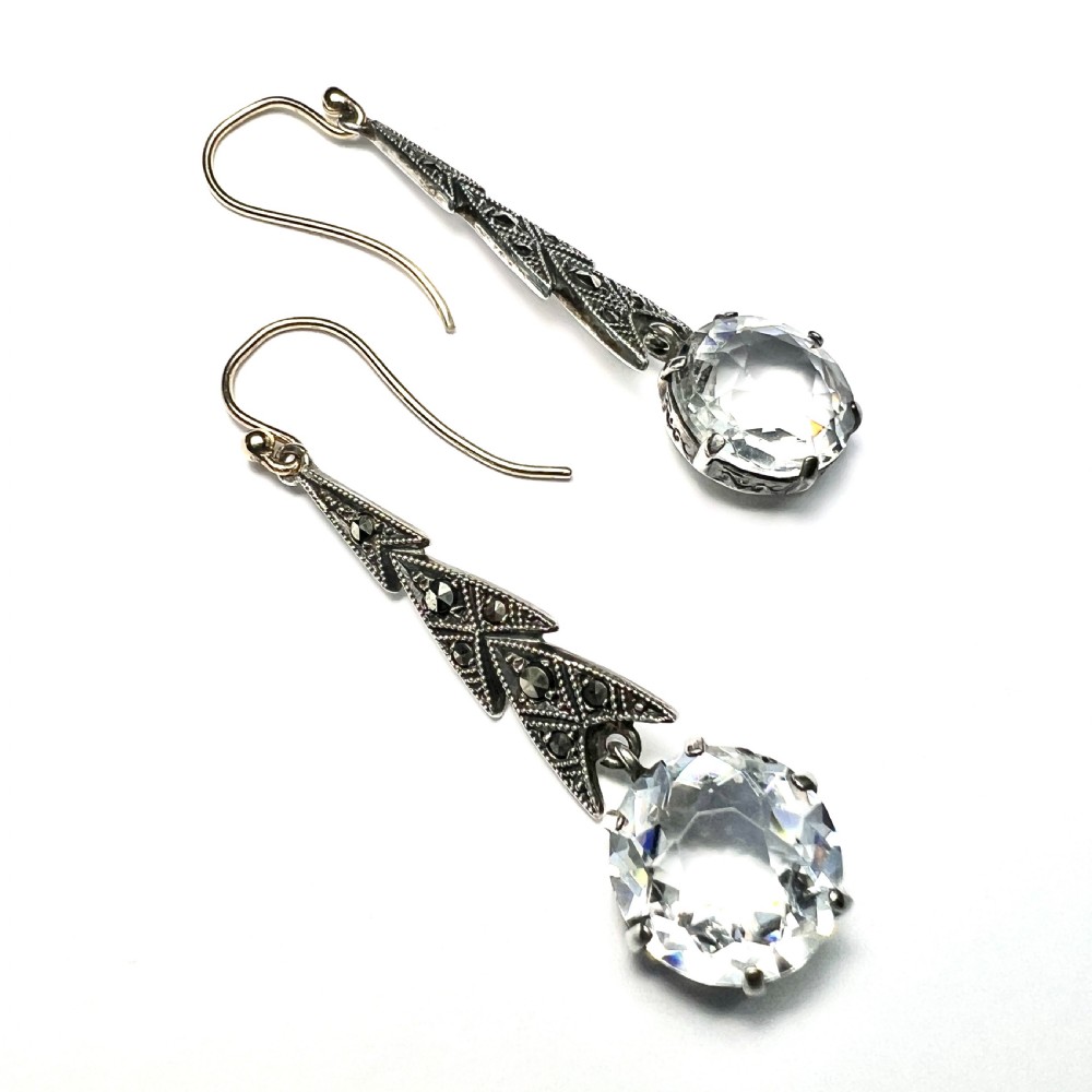Art Deco silver drop earrings featuring geometric marcasite-set chevron panels above large round faceted clear zircon stones. View VI