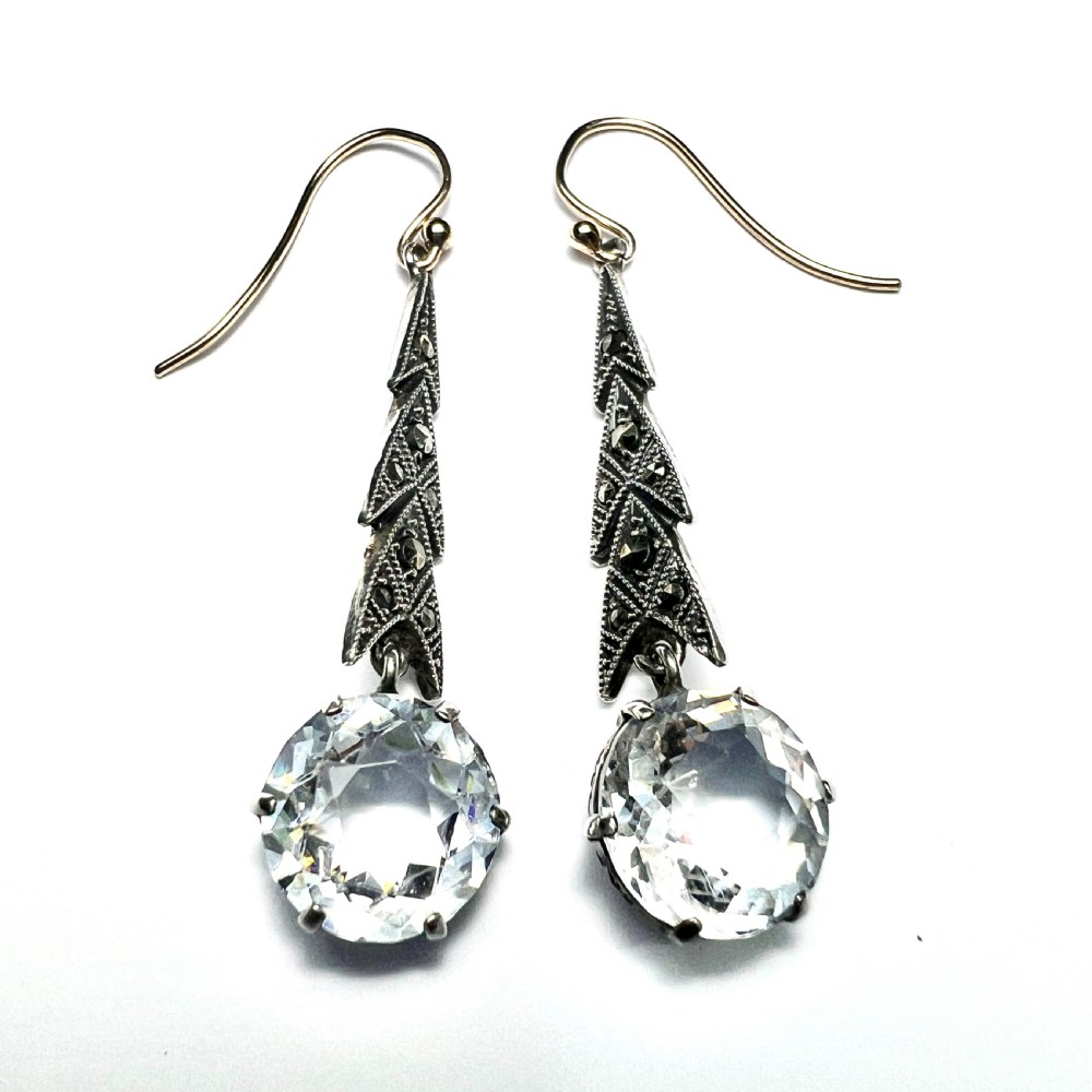Art Deco silver drop earrings featuring geometric marcasite-set chevron panels above large round faceted clear zircon stones. View VII