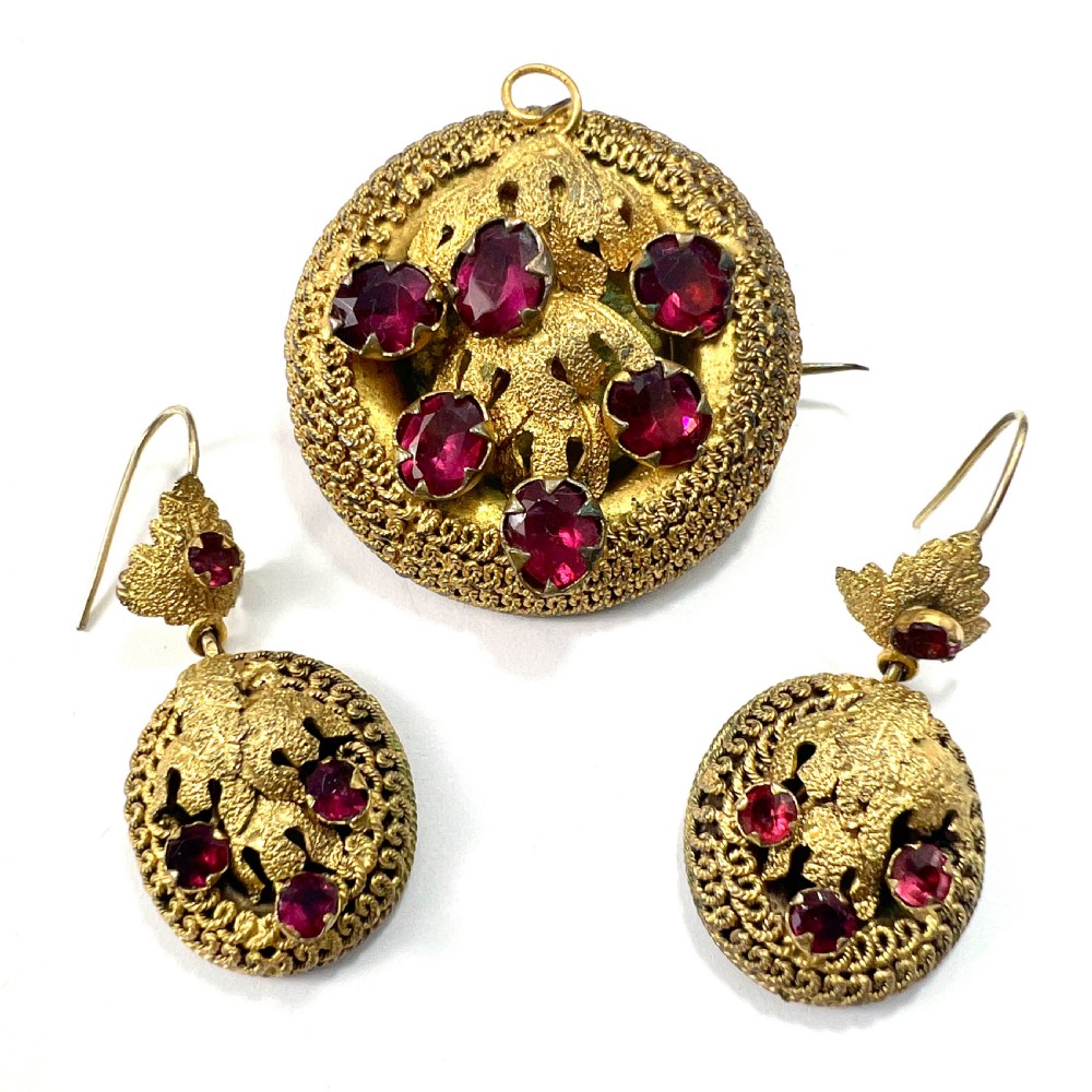 A Victorian Etruscan Revival jewellery set featuring a circular gilt brooch pendant and matching drop earrings set with faceted deep red paste stones.