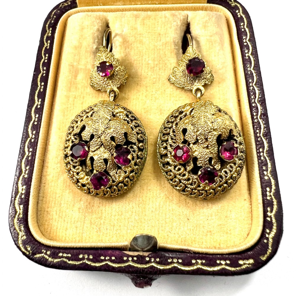 A Victorian Etruscan Revival jewellery set featuring a circular gilt brooch pendant and matching drop earrings set with faceted deep red paste stones. View II
