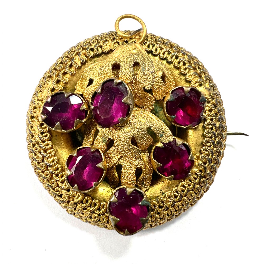 A Victorian Etruscan Revival jewellery set featuring a circular gilt brooch pendant and matching drop earrings set with faceted deep red paste stones. View III
