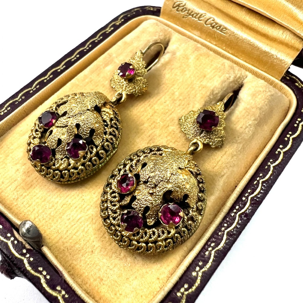 A Victorian Etruscan Revival jewellery set featuring a circular gilt brooch pendant and matching drop earrings set with faceted deep red paste stones. View V