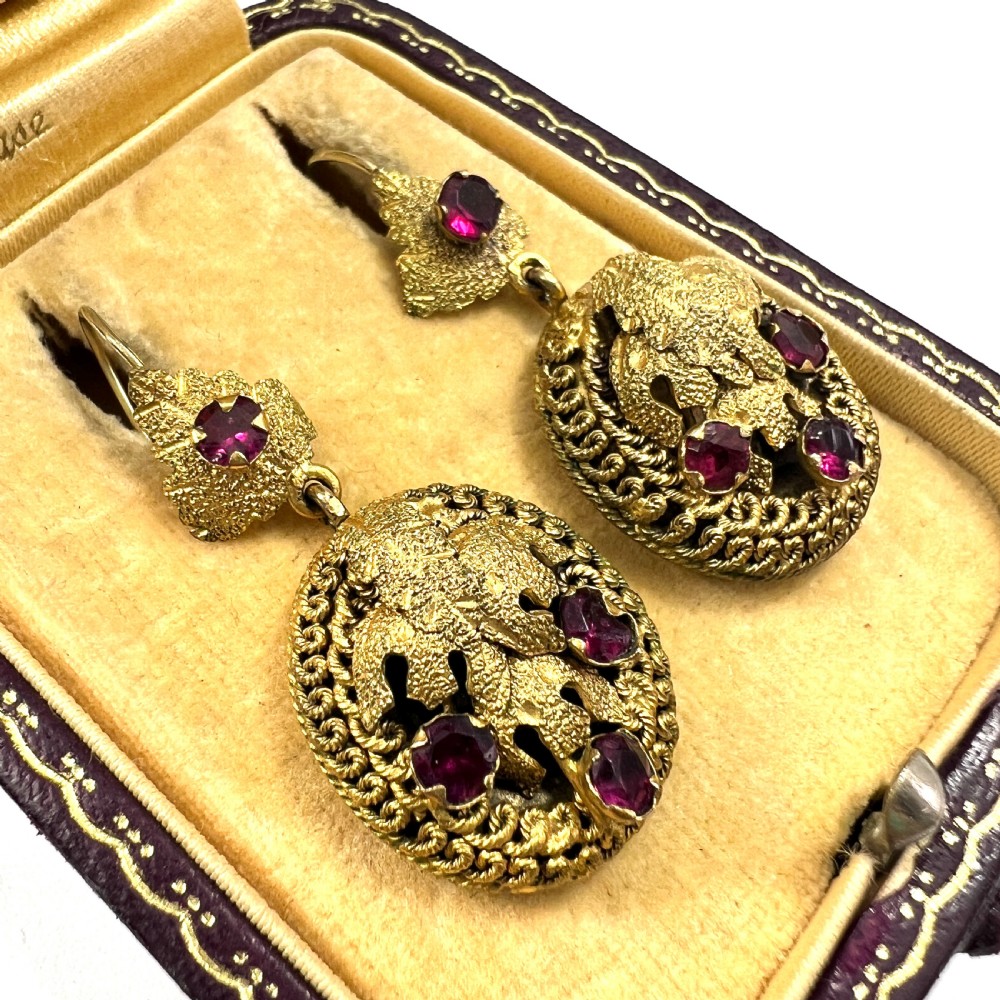 A Victorian Etruscan Revival jewellery set featuring a circular gilt brooch pendant and matching drop earrings set with faceted deep red paste stones. View VI