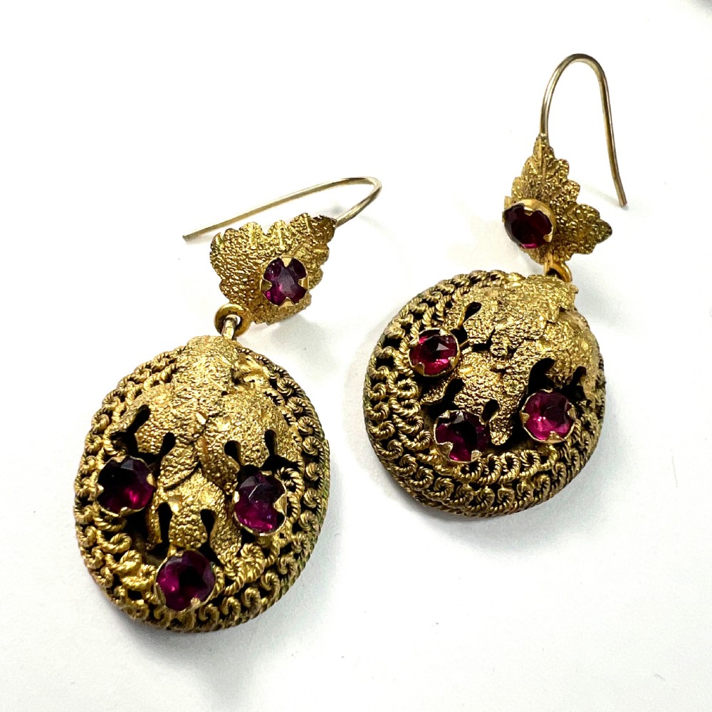 A Victorian Etruscan Revival jewellery set featuring a circular gilt brooch pendant and matching drop earrings set with faceted deep red paste stones. View VIII