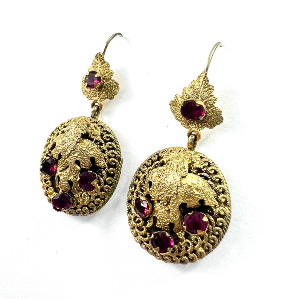 A Victorian Etruscan Revival jewellery set featuring a circular gilt brooch pendant and matching drop earrings set with faceted deep red paste stones. View IX