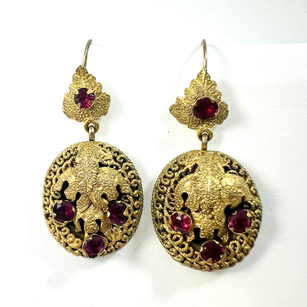A Victorian Etruscan Revival jewellery set featuring a circular gilt brooch pendant and matching drop earrings set with faceted deep red paste stones. View X