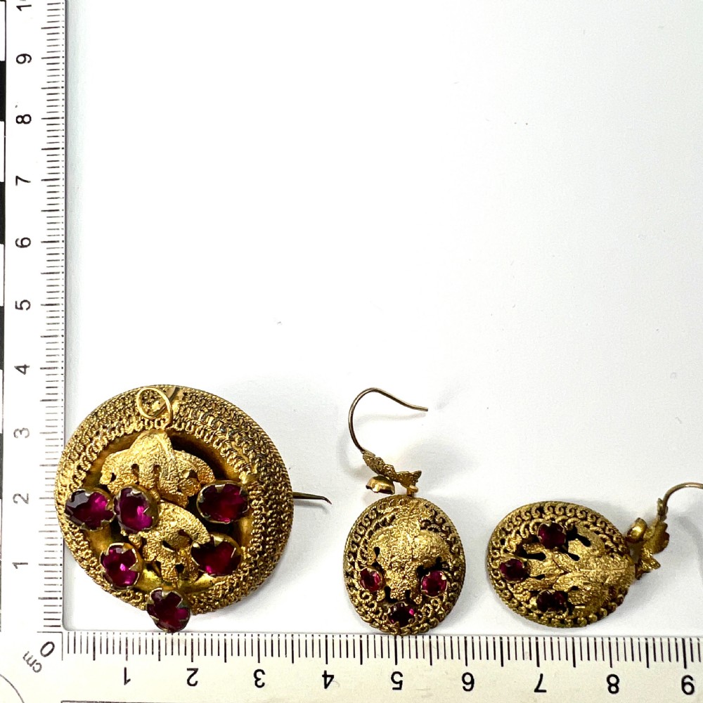 A Victorian Etruscan Revival jewellery set featuring a circular gilt brooch pendant and matching drop earrings set with faceted deep red paste stones. View XI