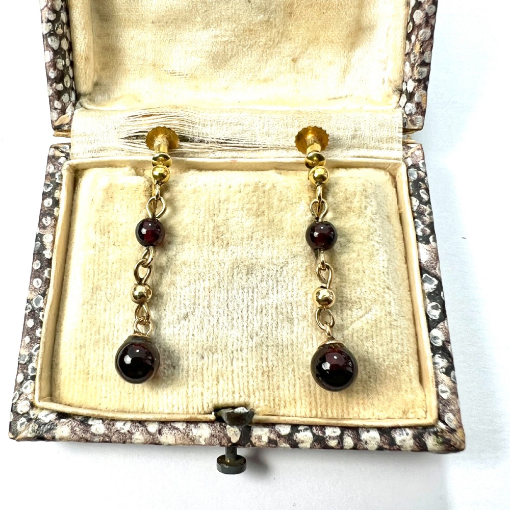 Pair of Edwardian 9ct yellow gold drop earrings with linked chains, spherical gold spacers, and polished dark red garnet beads on screw-back fittings.