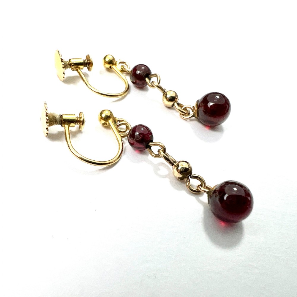 Pair of Edwardian 9ct yellow gold drop earrings with linked chains, spherical gold spacers, and polished dark red garnet beads on screw-back fittings. View IV