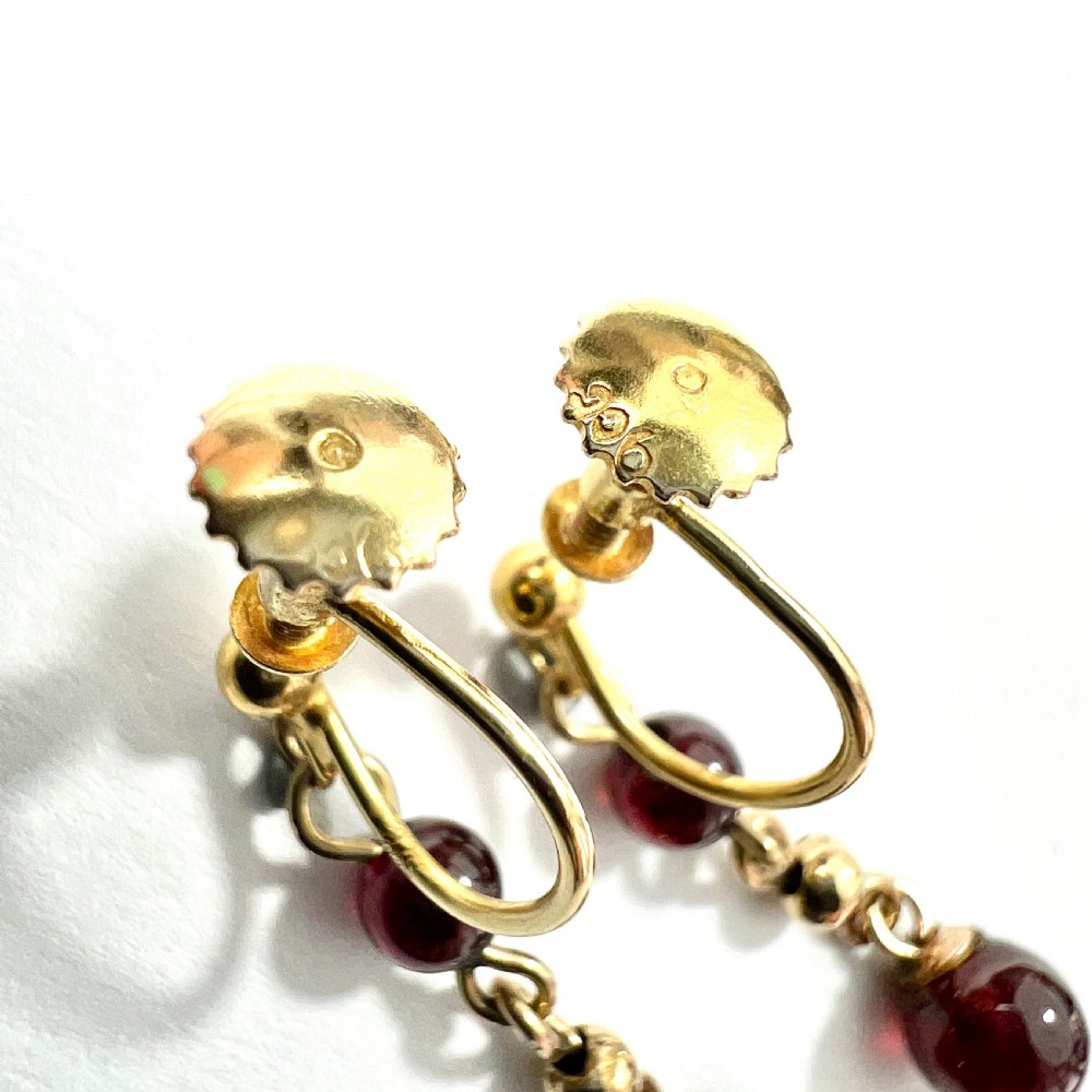 Pair of Edwardian 9ct yellow gold drop earrings with linked chains, spherical gold spacers, and polished dark red garnet beads on screw-back fittings. View VI