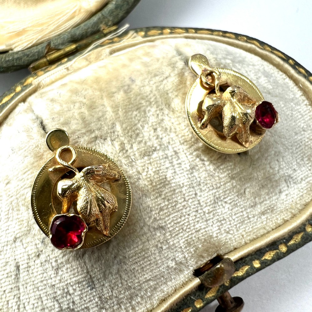 A pair of Victorian 18ct gold stud earrings featuring textured vine leaf motifs and circular red ruby accents set on round gold discs. View II