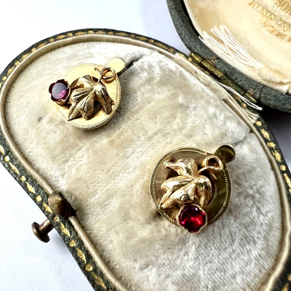 A pair of Victorian 18ct gold stud earrings featuring textured vine leaf motifs and circular red ruby accents set on round gold discs. View III