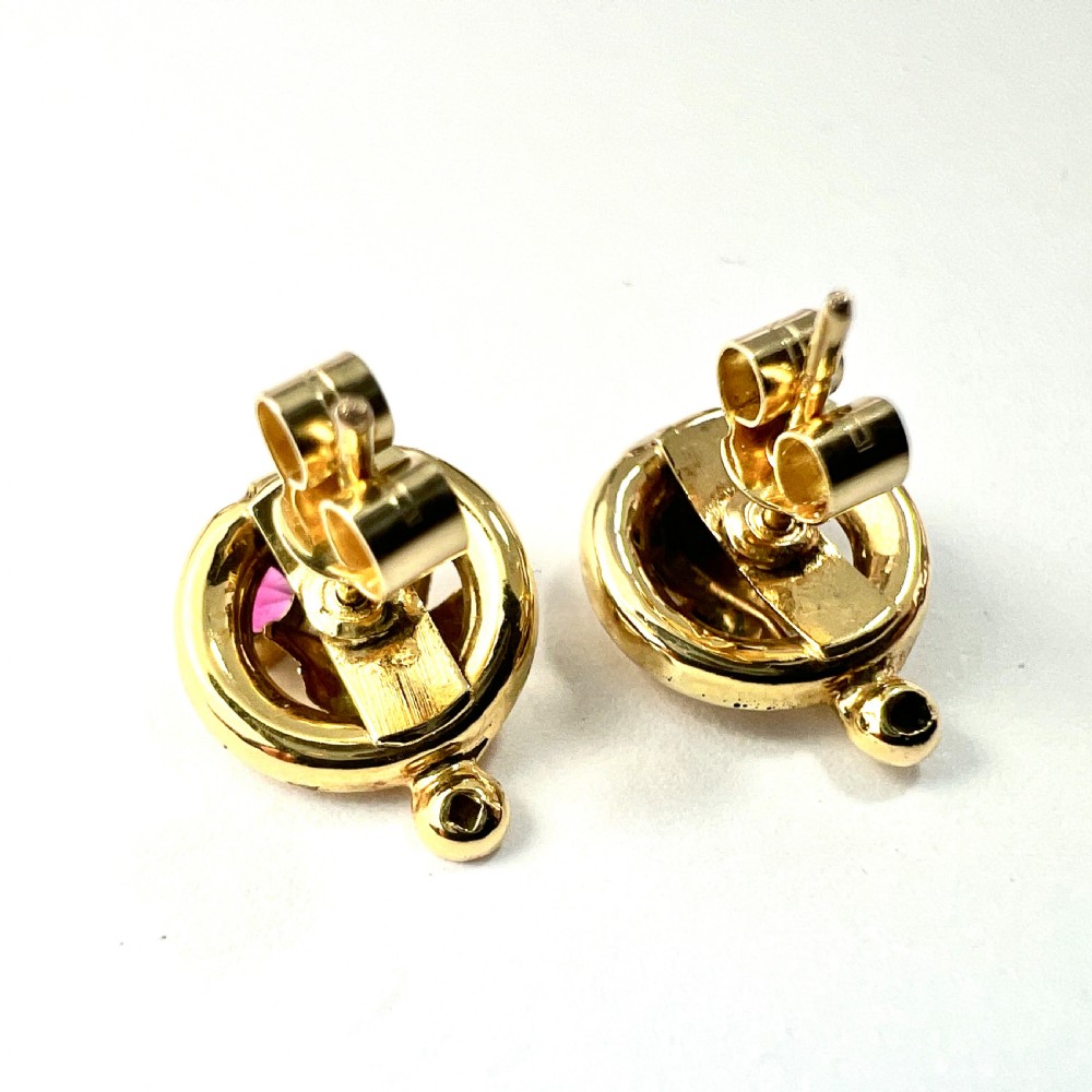 A pair of Victorian 18ct gold stud earrings featuring textured vine leaf motifs and circular red ruby accents set on round gold discs. View VI