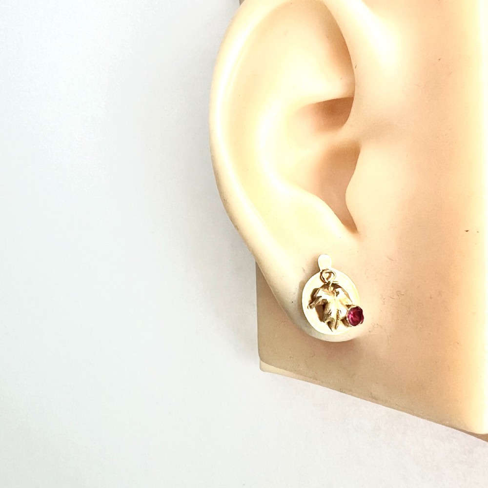 A pair of Victorian 18ct gold stud earrings featuring textured vine leaf motifs and circular red ruby accents set on round gold discs. View VII