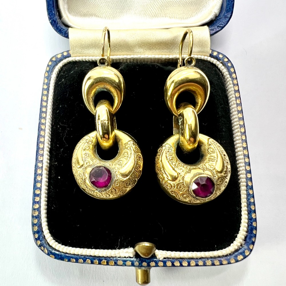 A pair of Victorian gold drop earrings featuring engraved hoop-shaped dangles inset with deep red garnet paste stones.