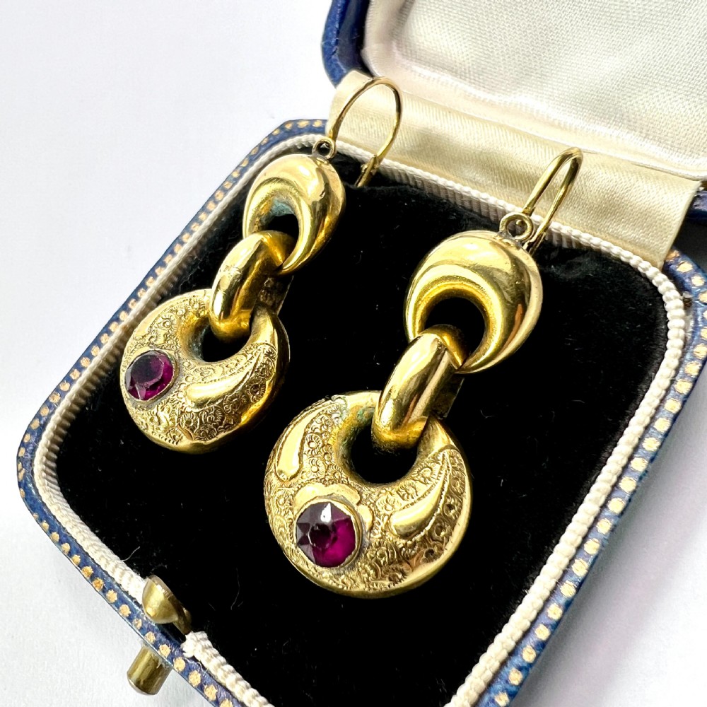 A pair of Victorian gold drop earrings featuring engraved hoop-shaped dangles inset with deep red garnet paste stones. View II