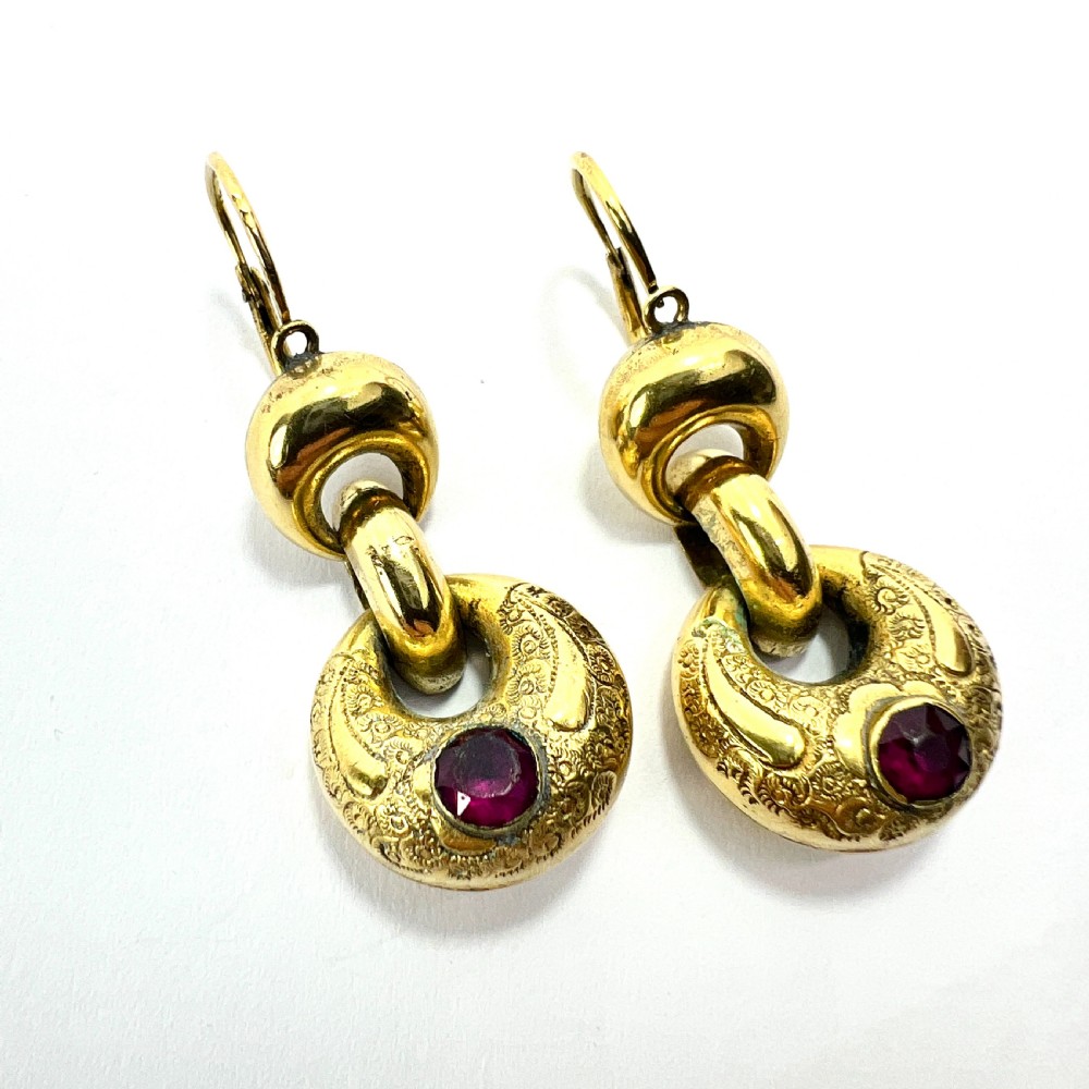A pair of Victorian gold drop earrings featuring engraved hoop-shaped dangles inset with deep red garnet paste stones. View V
