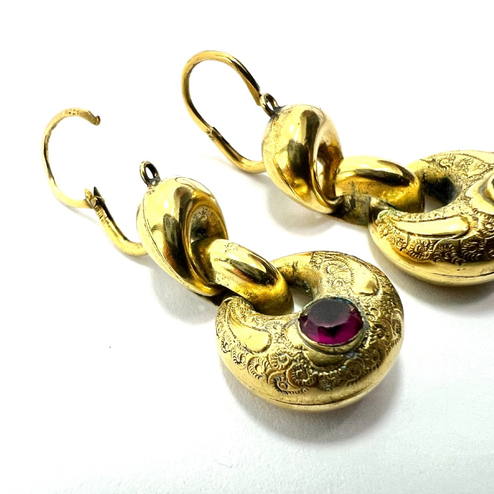 A pair of Victorian gold drop earrings featuring engraved hoop-shaped dangles inset with deep red garnet paste stones. View VI