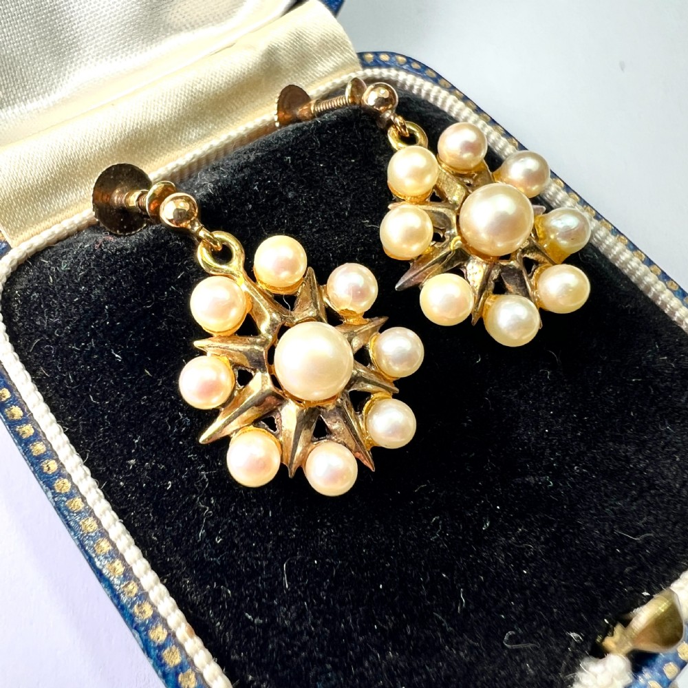 A pair of vintage 9ct gold screwback earrings featuring a central pearl surrounded by a sunburst frame set with smaller pearls.